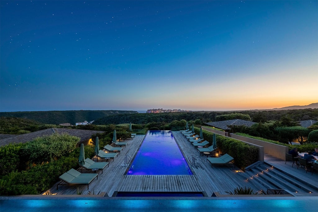 Modern luxury hotel nestled in Corsican hillside with infinity pool overlooking Mediterranean Sea, stone facades and lush gardens