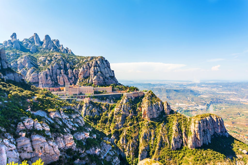 Spanish hillside monastery of Montserrat perched dramatically on rocky mountain peaks with lush forest surroundings and clouds below