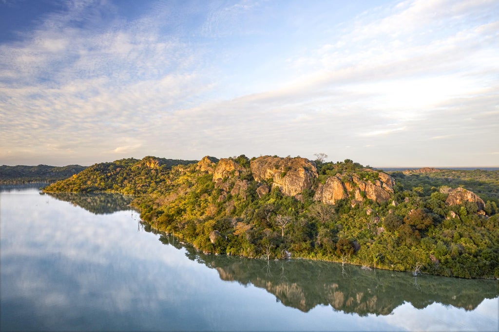 Luxury safari lodge perched on rocky hillside with infinity pool overlooking vast African savanna and Malilangwe Dam at sunset