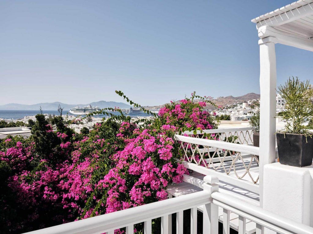 Luxurious white Cycladic-style hotel with infinity pool overlooking Mykonos bay, sunbeds and umbrellas lining azure waters