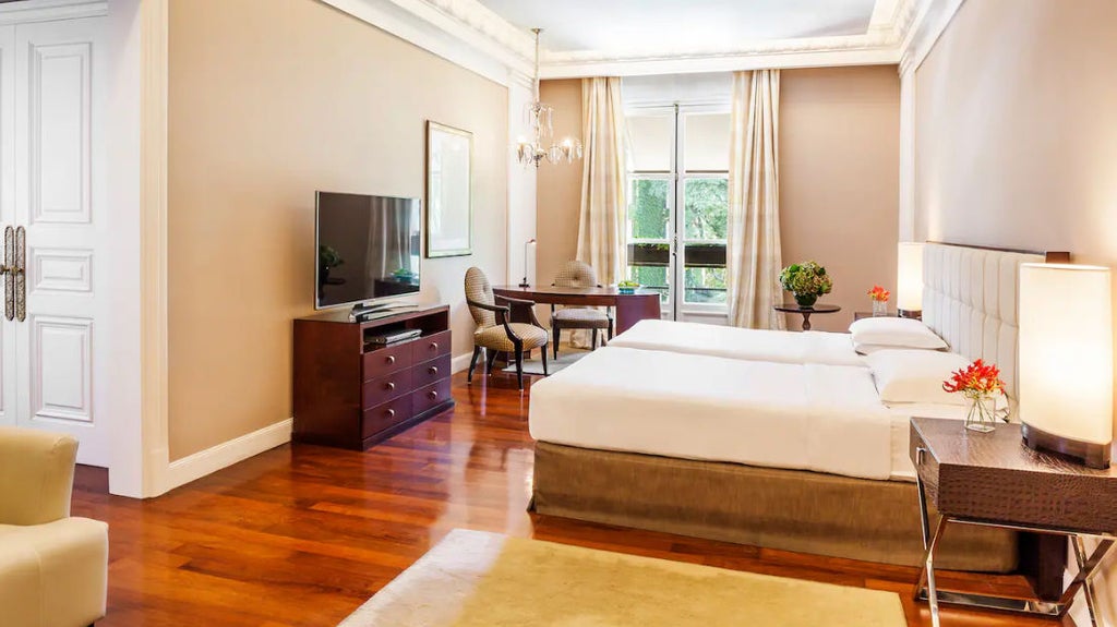 Elegant twin bedroom with crystal chandelier, plush cream headboards, marble finishes, and floor-to-ceiling windows overlooking Buenos Aires