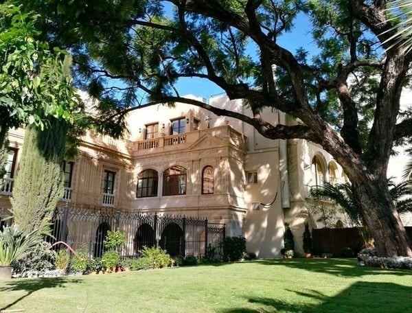 Grand 18th-century Spanish palace hotel with ornate stone facade, elegant balconies, and manicured gardens under blue skies