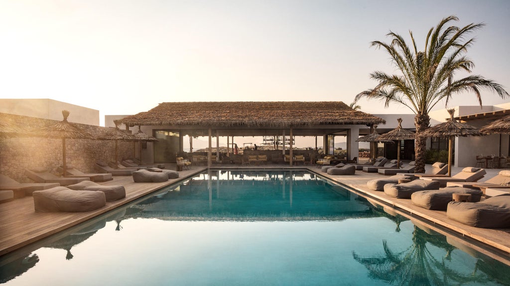 Luxury beachfront resort with whitewashed buildings, infinity pool overlooking the Aegean Sea, and minimalist Mediterranean architecture