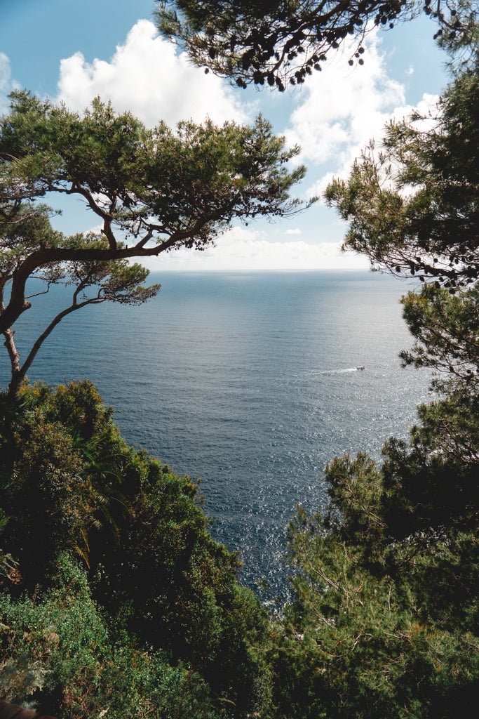 Steep cliffs rise above crystal-clear turquoise waters along Corsica's dramatic coastline, with a luxury yacht anchored in a secluded cove