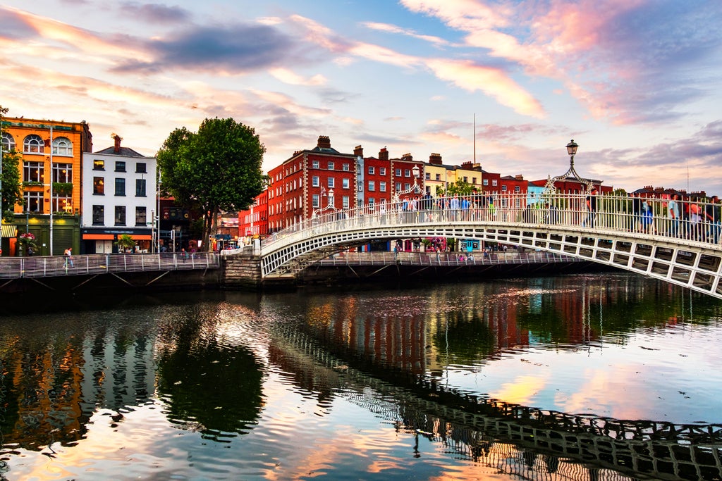 Sunset view of Dublin's iconic Ha'penny Bridge spanning River Liffey, with illuminated Georgian buildings and quays reflected in calm waters