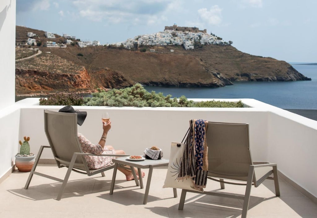 Elegant white and blue honeymoon suite with panoramic Aegean Sea view, minimalist design, private balcony, and classic Greek island architecture.