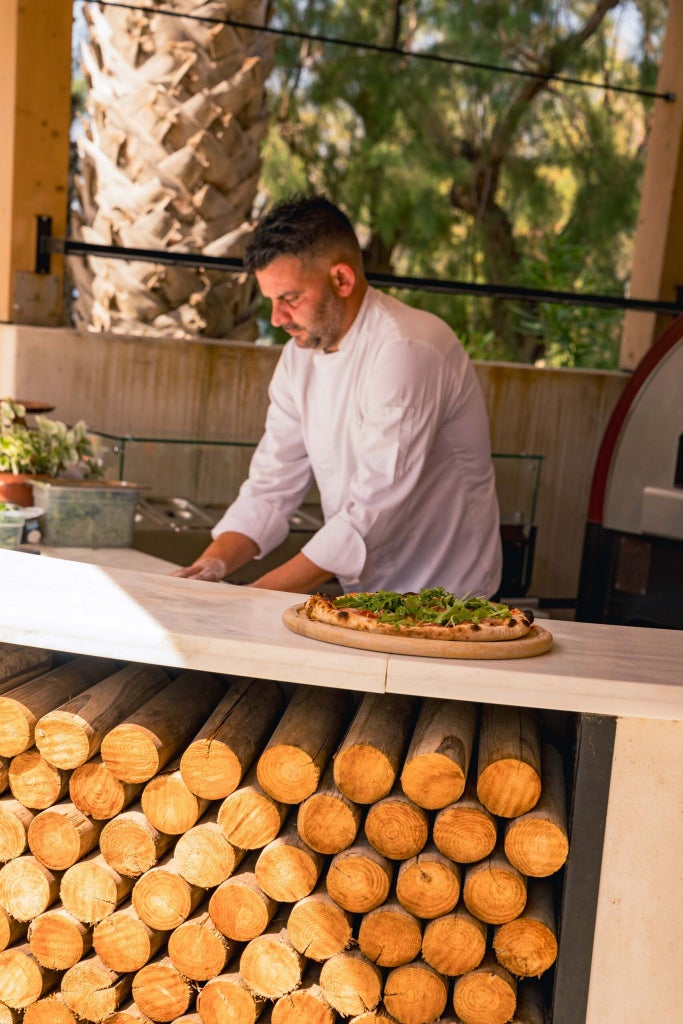 Luxurious beachfront resort with white-washed buildings, azure pools, and palm trees overlooking the crystal-clear waters of the Cretan coastline at scenset.