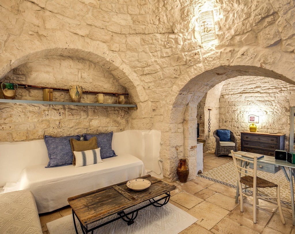 Rustic-chic junior suite with exposed stone walls, elegant white linens, and warm wooden furniture in a traditional Italian masseria setting