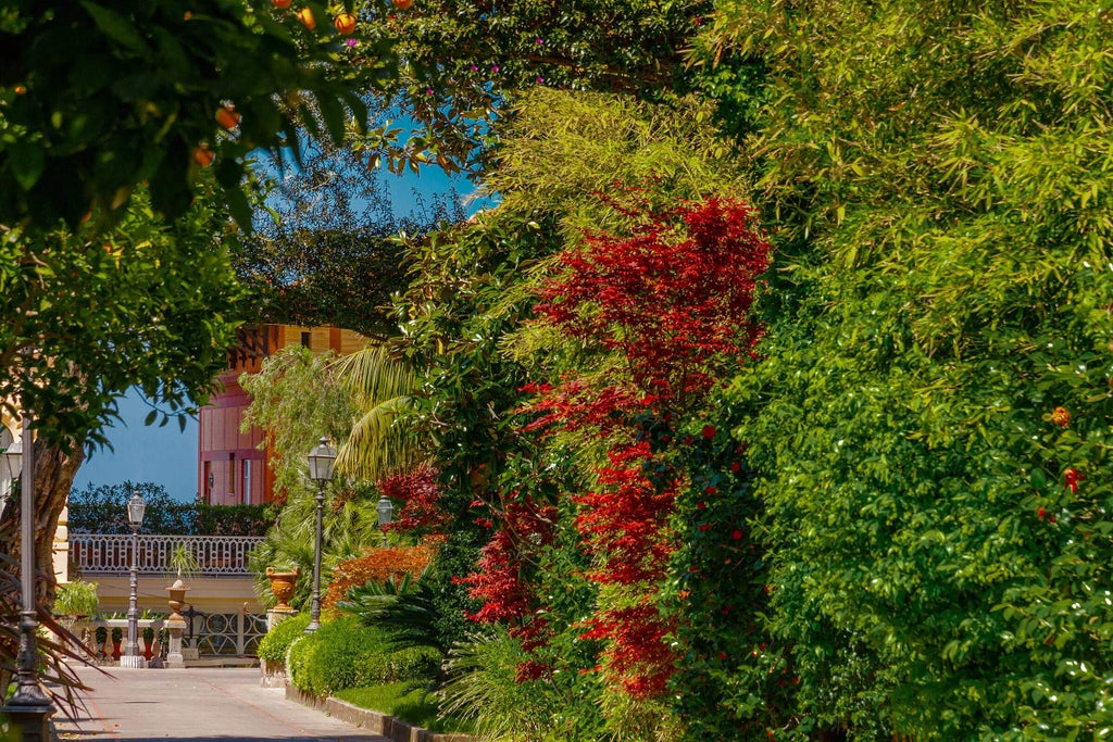 Historic luxury hotel with ornate cream facade, arched windows and balconies, nestled among lush Mediterranean gardens overlooking Sorrento Bay