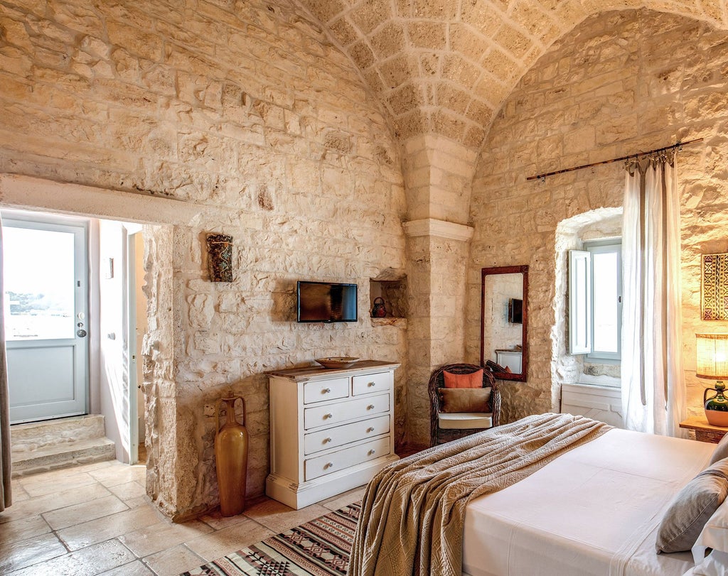 Rustic stone walls, elegant white linens, and warm wooden furnishings define this luxurious Superior room at Masseria Cervarolo in scenic Puglia, Italy.