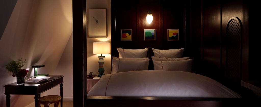 Elegant Parisian hotel room with plush bedding, dark moody walls, minimalist design, and soft ambient lighting reflecting sophisticated boutique aesthetic