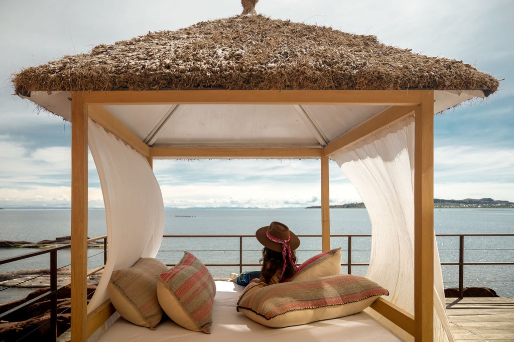 Modern luxury lodge with floor-to-ceiling windows overlooking Lake Titicaca, featuring a stone facade and scenic waterfront terrace at sunset