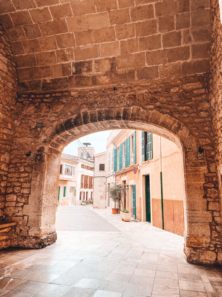 Elegant Mallorcan stone hotel with traditional Spanish architecture, featuring arched windows and a serene courtyard pool lined by palm trees