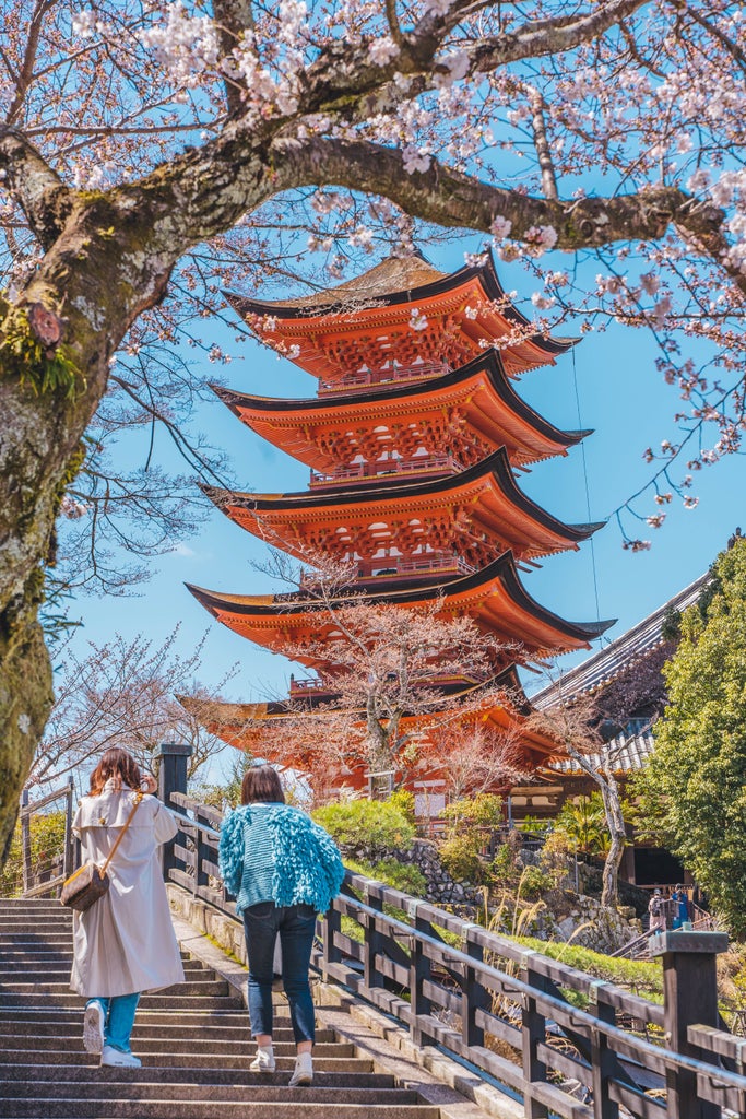 Majestic orange torii gate standing in water during sunset at Miyajima, with Mount Misen rising behind and temple roofs visible