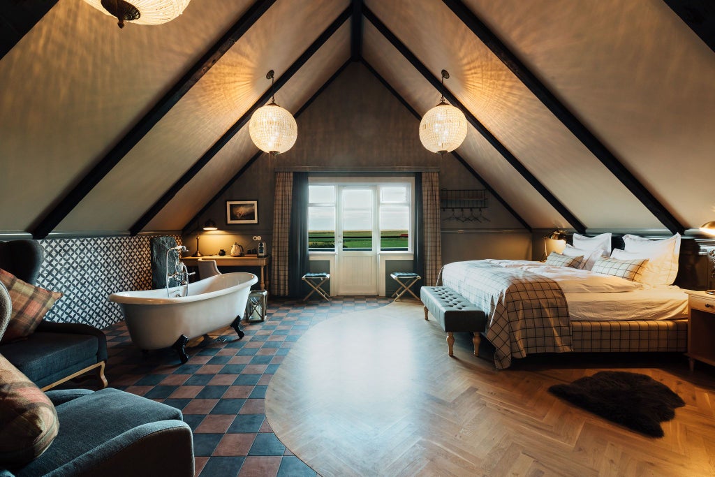 Elegant mini suite at Skálakot Manor Hotel with plush white bedding, wooden floors, and panoramic Icelandic landscape view through large windows