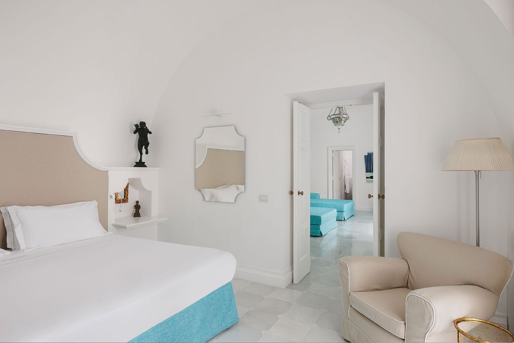 Elegant coastal suite with panoramic Mediterranean views, luxurious white decor, plush king bed, and expansive glass doors overlooking Sorrento's dramatic cliffs