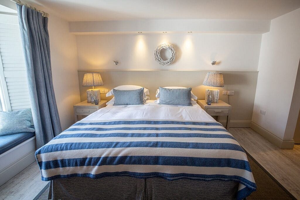 Elegant seaside village room with crisp white linens, nautical blue accents, and panoramic coastal views of St Mawes, showcasing refined maritime charm and comfort.