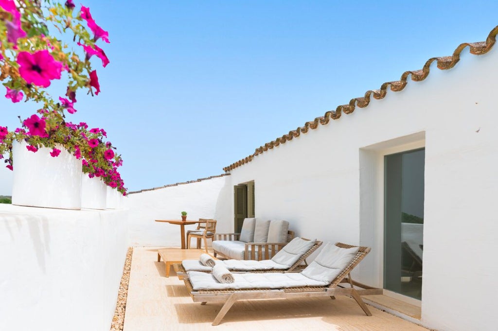 Elegant whitewashed stone hotel room with minimalist design, soft linens, and panoramic view of Mediterranean landscape in Menorca, Spain.