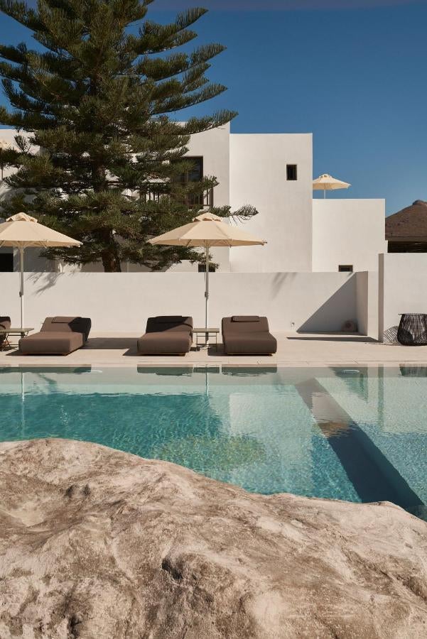 White luxury boutique hotel in Paros, Greece with minimalist architecture, arched doorways and bougainvillea flowers against blue sky