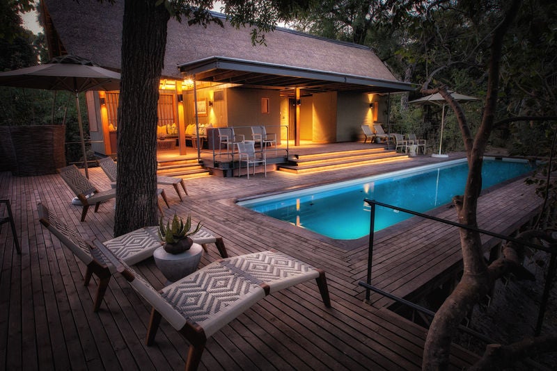 Elevated luxury safari tent overlooking vast grasslands in Okavango Delta, surrounded by acacia trees and natural waterways