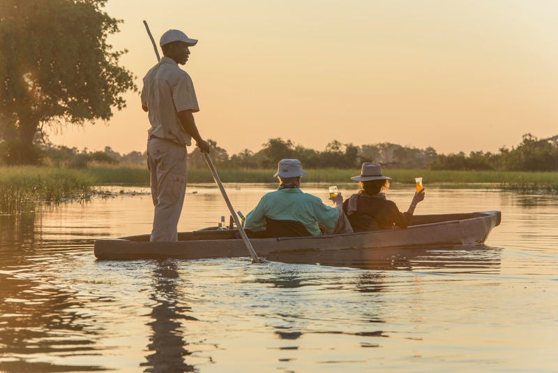 Elevated luxury safari lodge with thatched-roof suites perched on wooden stilts above wetlands in Botswana's Okavango Delta