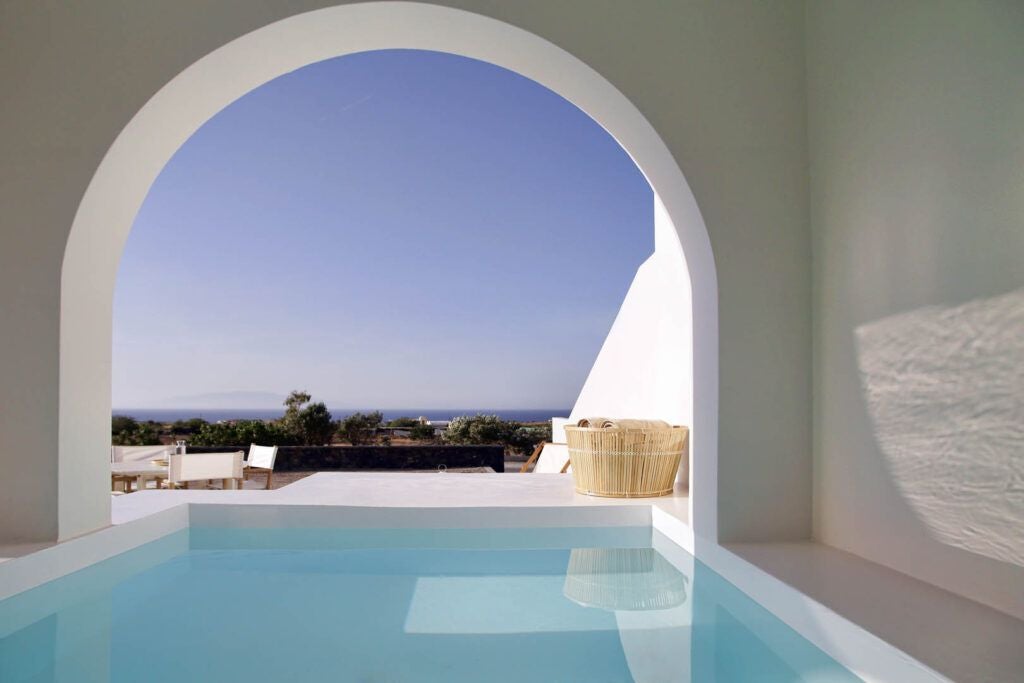 Luxurious white-washed Greek villa with blue-domed roofs overlooking azure Aegean Sea, traditional Cycladic architecture nestled on scenic hillside