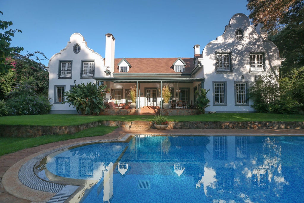 Elegant colonial-style mansion with ornate wooden balconies, surrounded by lush tropical gardens and palm trees in Nairobi's suburbs