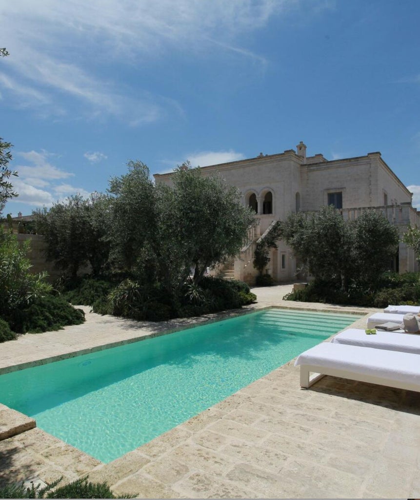 Elegant Mediterranean hotel suite with stone walls, vaulted ceiling, freestanding bathtub, and luxurious cream furnishings bathed in natural light