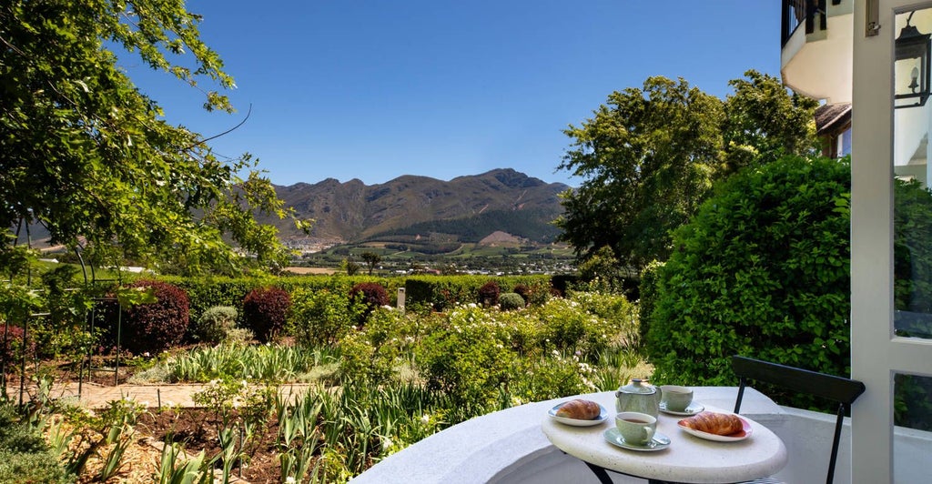 Luxurious wine country suite with king bed, elegant wood furnishings, and panoramic mountain views at a high-end vineyard hotel in South African landscape