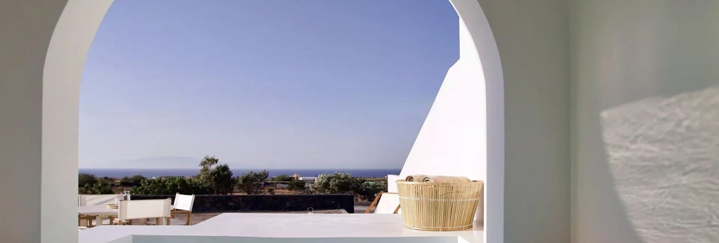 Luxurious Mediterranean villa bedroom with whitewashed walls, elegant wooden furniture, and panoramic view of scenic Greek landscape through large windows