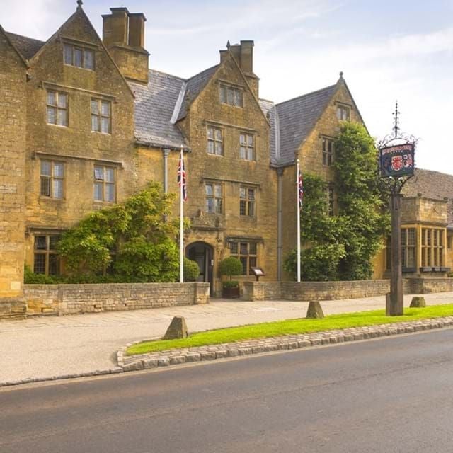 Elegant stone exterior of historic luxury hotel with ivy-covered walls, traditional British architecture, and pristine landscaped gardens at The Lygon Arms.