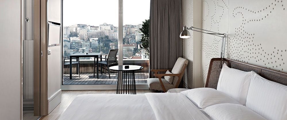 Modern luxury hotel room with panoramic city view, spacious terrace, sleek contemporary design, and elegant queen-sized bed overlooking [Scenset] skyline in Turkey