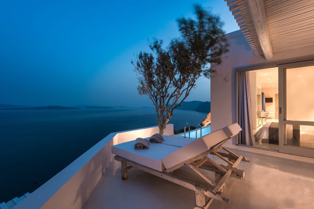 Luxurious white-washed Santorini hotel featuring a curved infinity pool overlooking the Aegean Sea and dramatic caldera cliffs at sunset