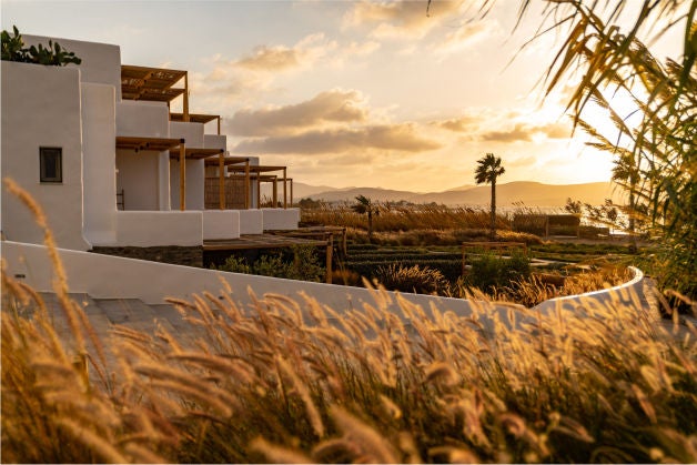 Elegant whitewashed Greek hotel with infinity pool overlooking Aegean Sea, cascading terraces and traditional blue domed rooftops