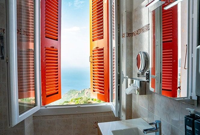 Minimalist seaside hotel room with white linens, blue Mediterranean views, and mid-century modern furniture at scenic coastal French resort