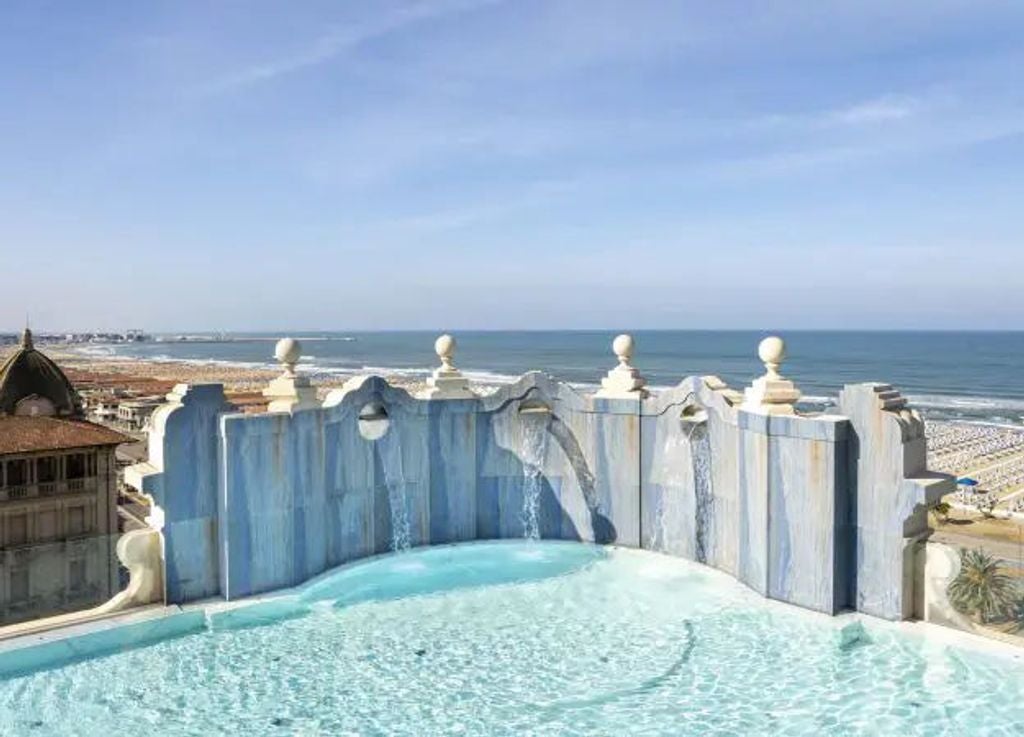 Elegant five-story luxury hotel with classic Italian architecture, ornate stone balconies, and symmetric windows overlooking the Viareggio coast