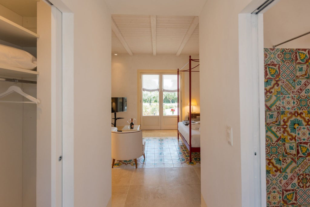 Luxurious Sicilian hotel room with soft white linens, elegant wooden furniture, and large windows overlooking lush Mediterranean garden landscape near Palma.