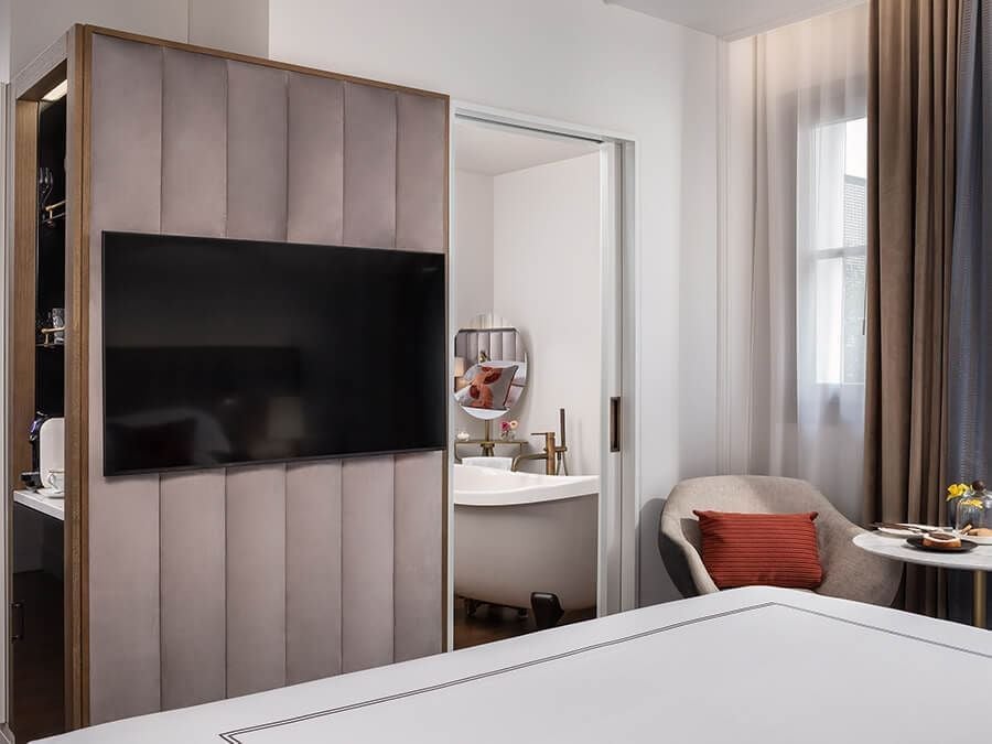 Elegant Gran Hotel Inglés Grand Deluxe Room with plush white linens, classic Spanish décor, and large windows overlooking historic Madrid streetscape