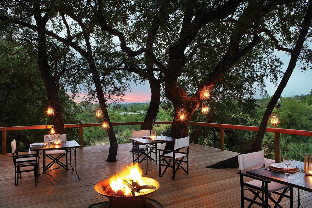 Elevated wooden luxury safari lodge nestled in acacia trees with private deck overlooking African savanna at golden hour