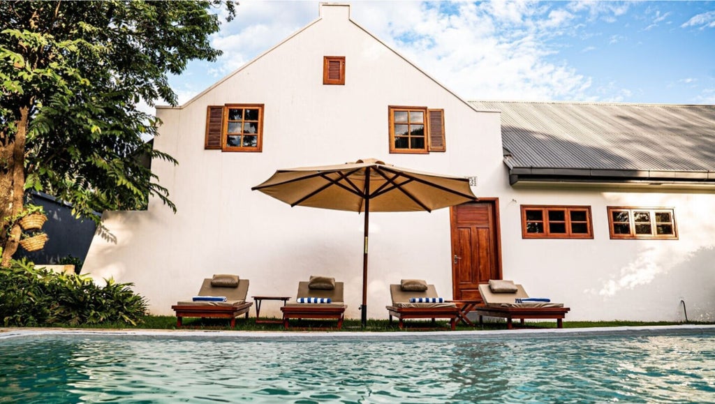 Elegant stone villa nestled in lush Tanzanian garden, with wraparound veranda, thatched roof, and mountain views at golden hour