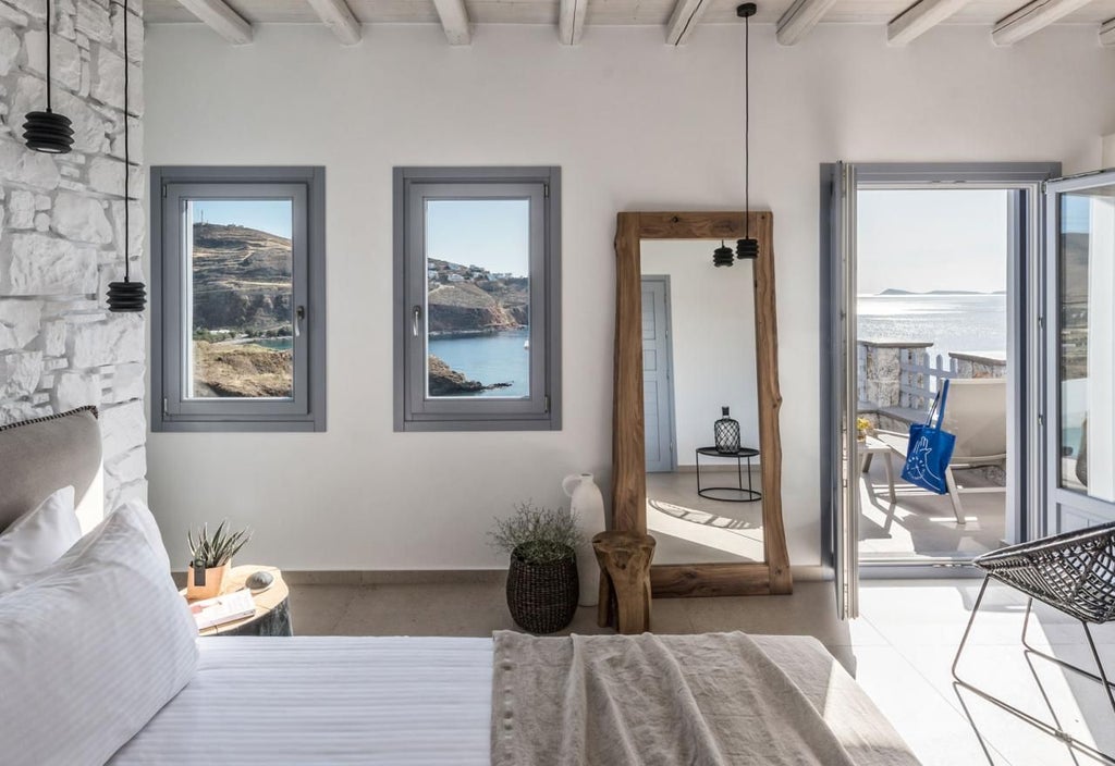 Elegant Cycladic-style honeymoon suite with white minimalist decor, private balcony overlooking azure Aegean Sea, plush king bed, and luxurious marble bathroom