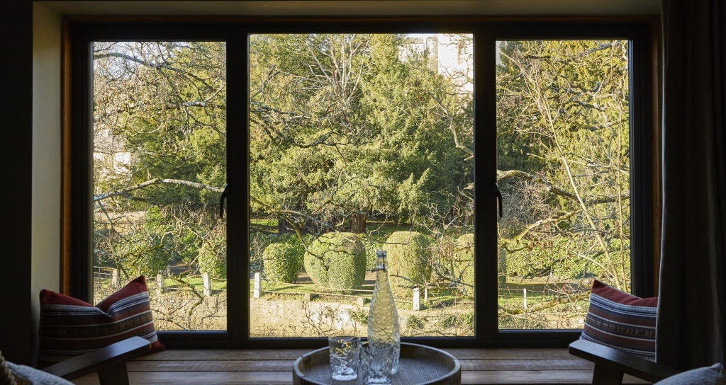 Elegant stone-built hotel nestled in picturesque United Kingdom countryside, featuring traditional architectural charm and inviting riverside terrace with lush greenery.