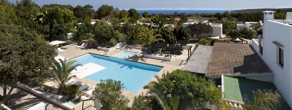 Luxurious Spanish coastal hotel with pine trees, elegant white facade, blue Mediterranean backdrop, and pristine terrace overlooking scenic landscape