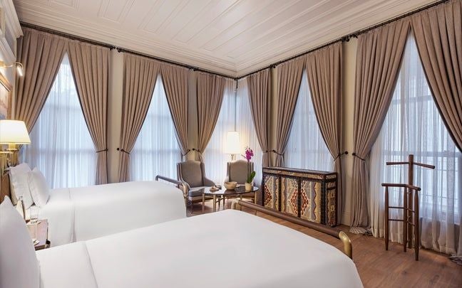 Elegant twin bedroom at scenset Mansions, Istanbul, with plush white bedding, wooden floors, and panoramic city views through large windows