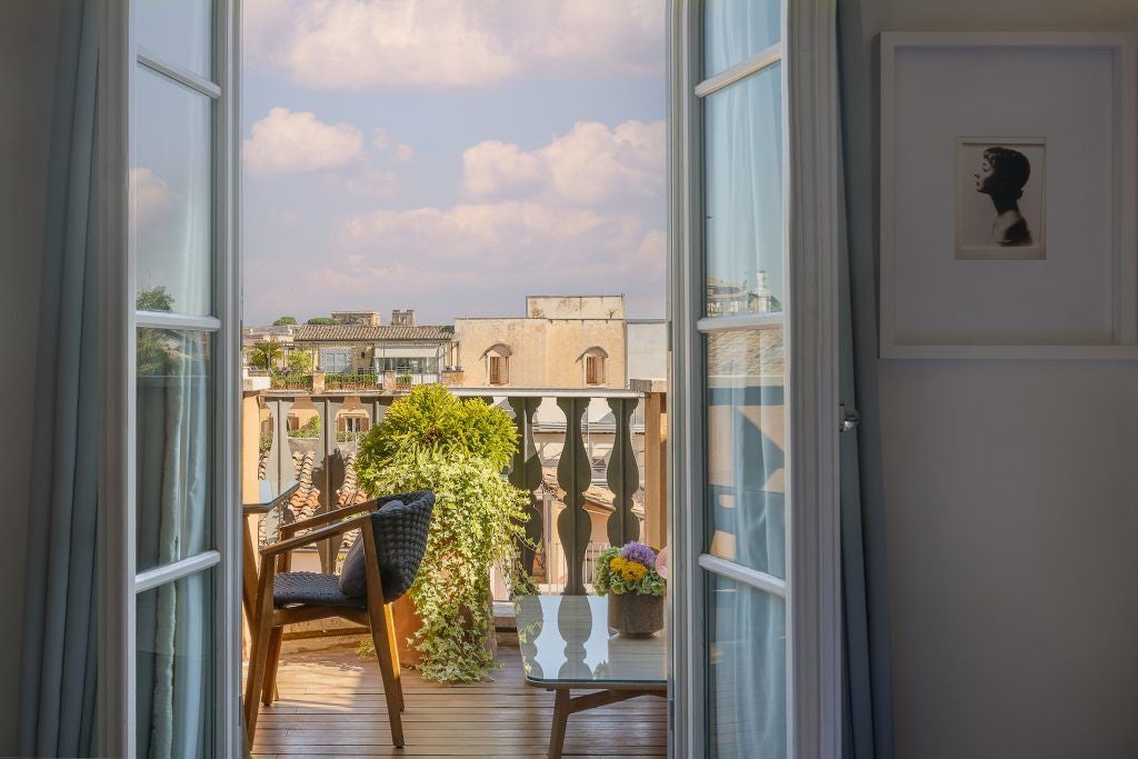 Elegant Studio Deluxe room at Portrait Roma with soft cream tones, modern furnishings, spacious terrace overlooking historic Italian cityscape at sunset