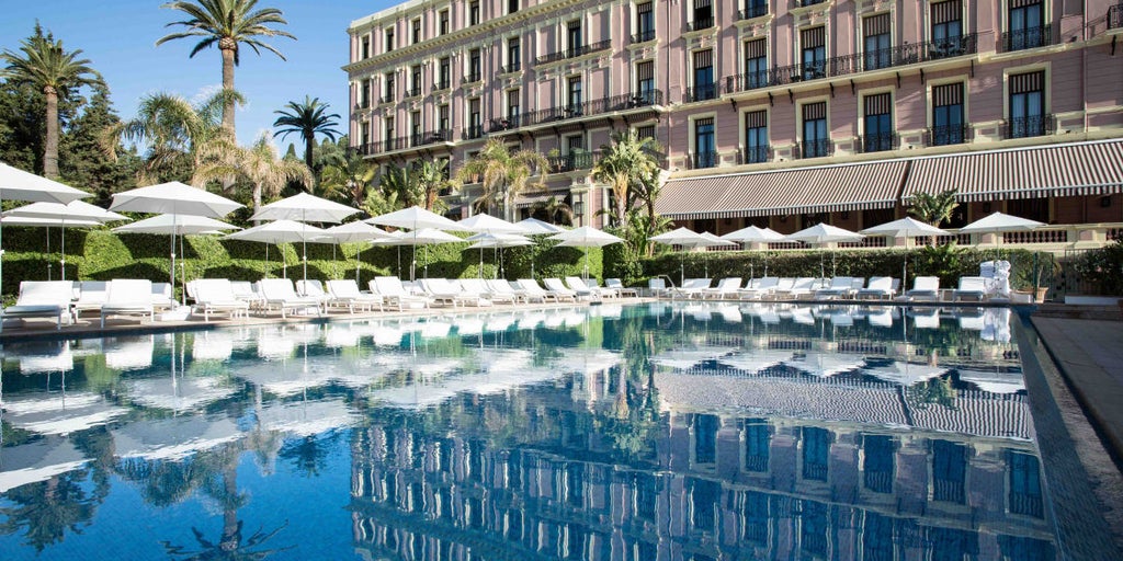 Five-star French Riviera hotel with elegant white facade, Mediterranean gardens, sea views, and a luxurious beachfront swimming pool