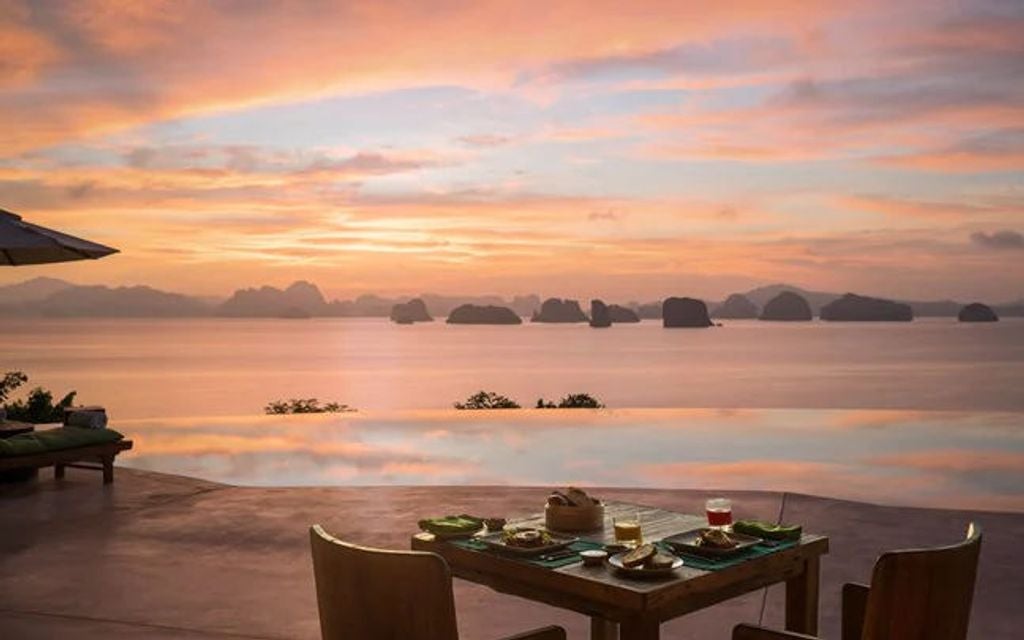 Luxurious overwater villa with private infinity pool overlooking limestone cliffs and emerald waters of Thailand's Phang Nga Bay at sunset