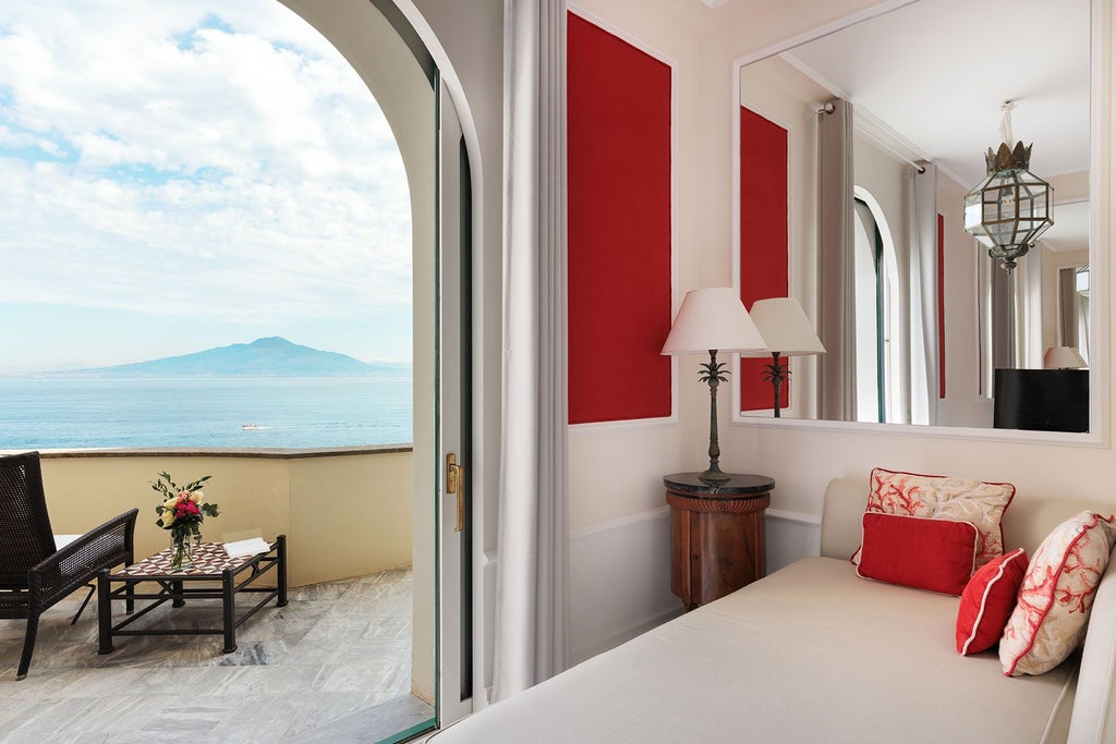 Luxurious coral-toned suite with panoramic Mediterranean views, elegant white furnishings, and ornate Italian coastal design at Bellevue Syrene hotel