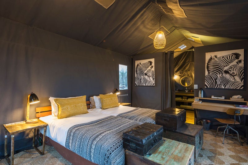 Luxurious elevated safari tent with wooden deck overlooking Botswana wilderness, surrounded by lush vegetation at golden hour