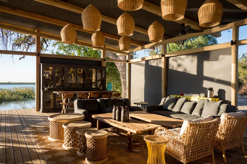 Contemporary safari tent with private deck overlooking pristine Linyanti wetlands, surrounded by acacia trees at sunset in Botswana